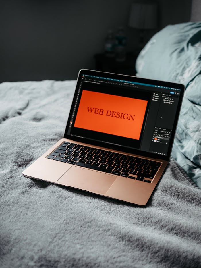hero-img A laptop on a bed showing web design software, creating a cozy workspace.